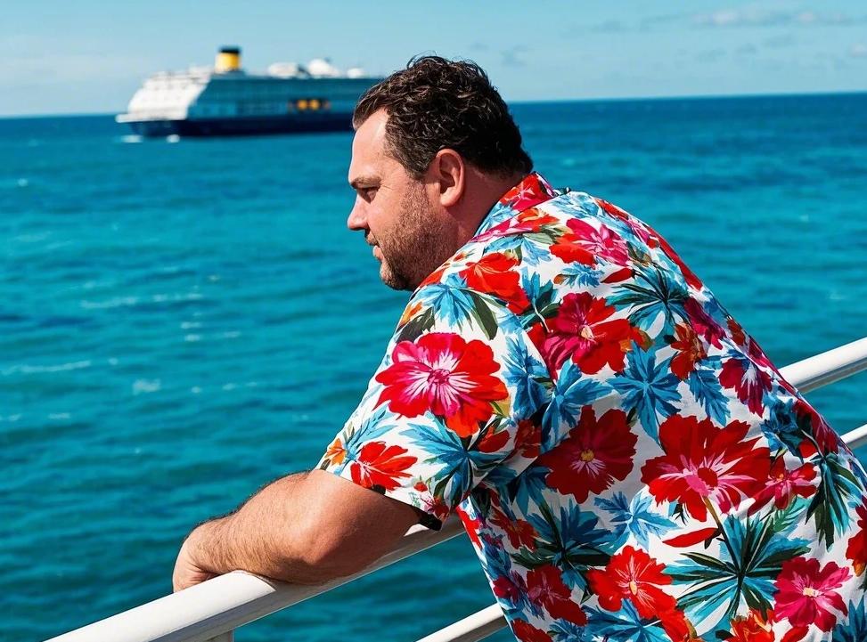 A fat man wearing a men's big and tall Hawaiian shirt on a cruise ship.