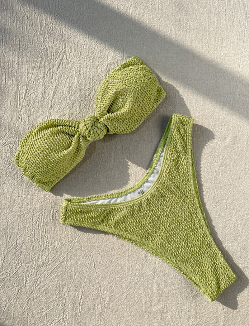 A green knitted bandeau bikini top laid flat, showcasing its texture and design.