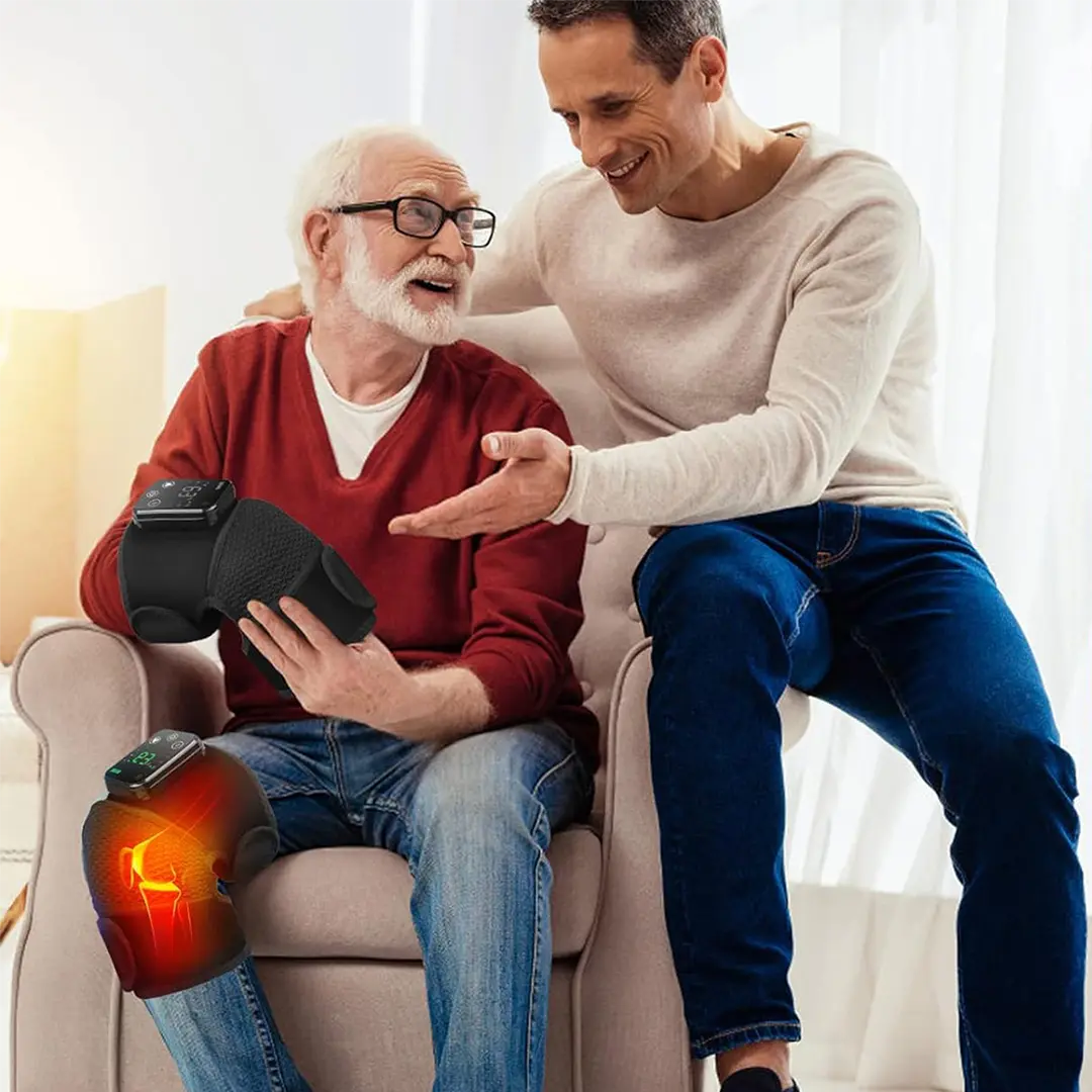 A younger man is pointing at a knee brace on an older man's leg while both are smiling.