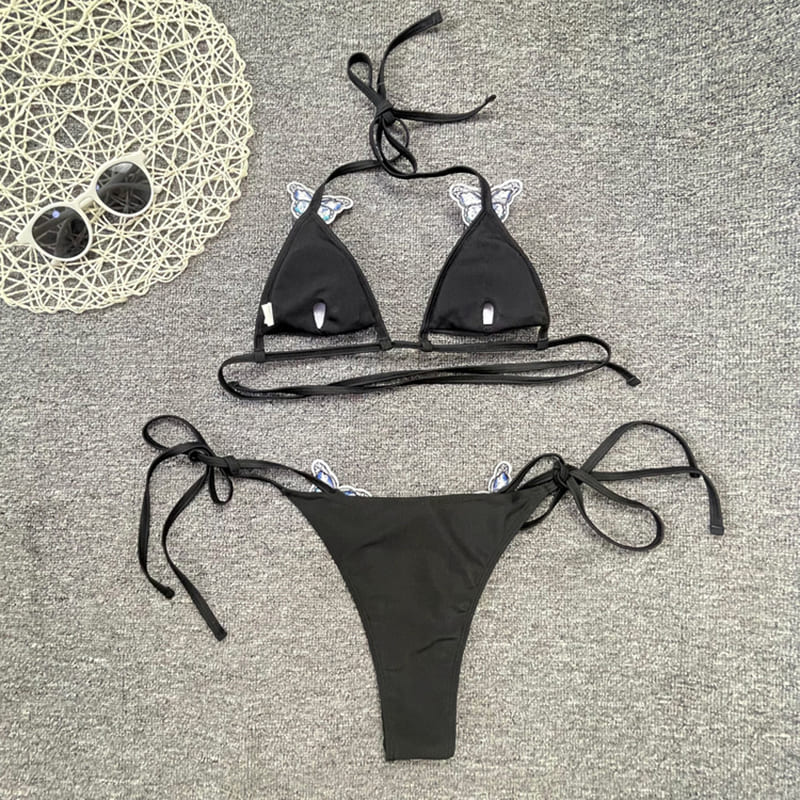 Flat lay back photo of a black bikini with a blue butterfly pattern on the bikini. The bikini is laid out to show the adjustable straps and side ties.