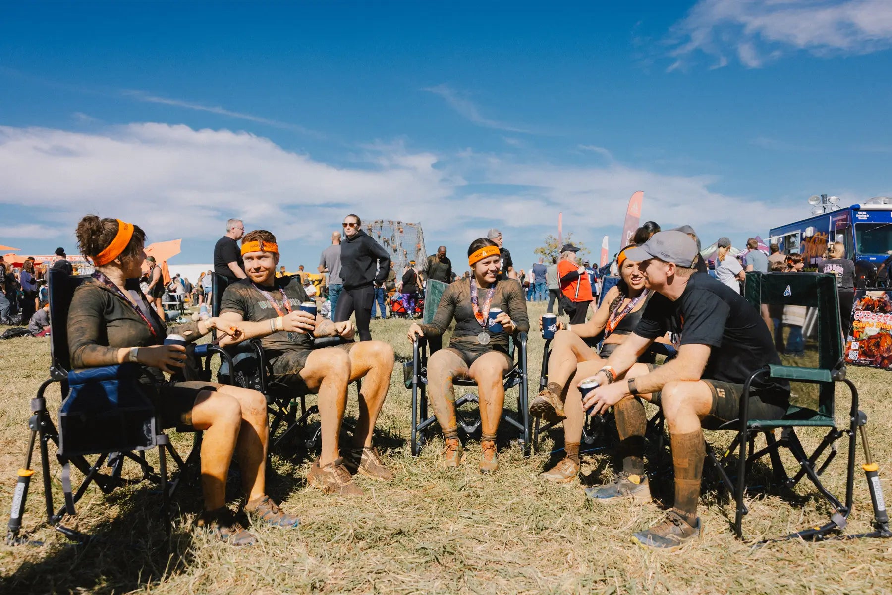 Group of muddy race finishers relaxing in Stowaway Rocker chairs at an outdoor event.