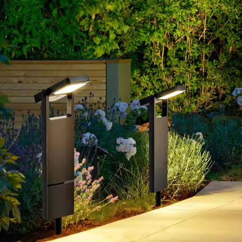 Two modern solar garden lights illuminating a landscaped pathway with flowers and greenery in the background.
