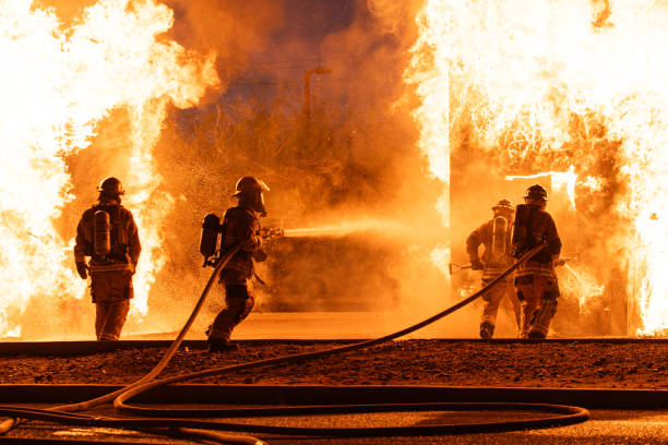 Firefighters Battling a Roaring Fire 4 firefighters battle a roaring blaze.  2 fire hoses shooting water. American Firefighter stock pictures, royalty-free photos & images
